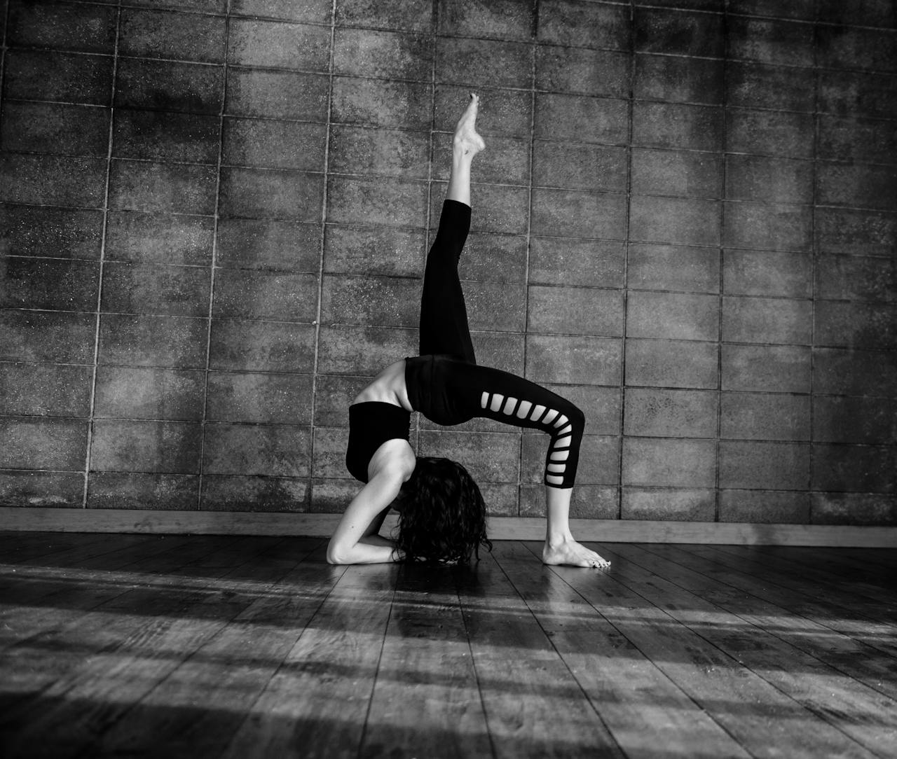 our-story Black and white image of a woman performing a gymnastic pose indoors.