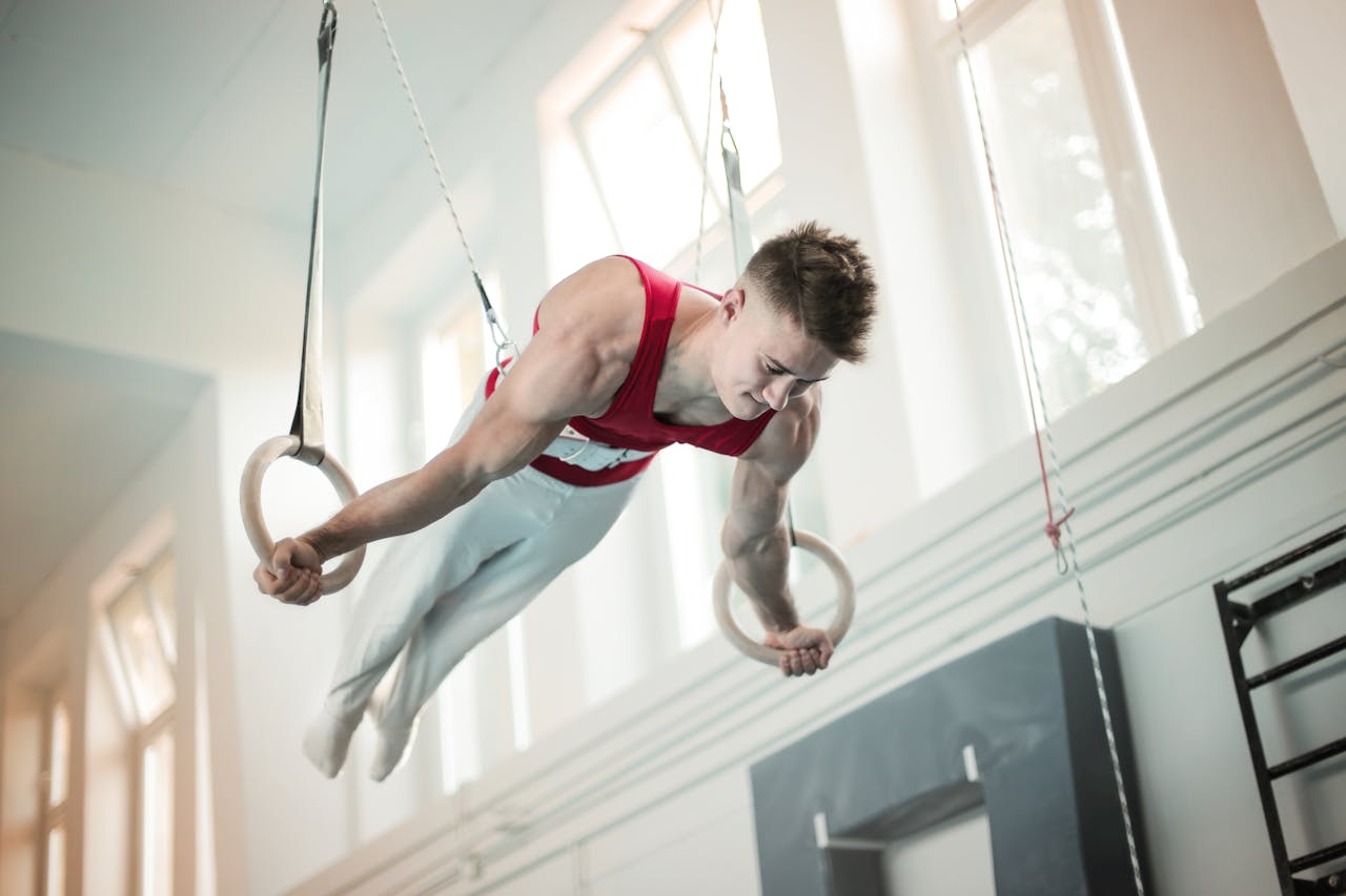 A male gymnast showcases strength and balance on rings during practice inside a gym.